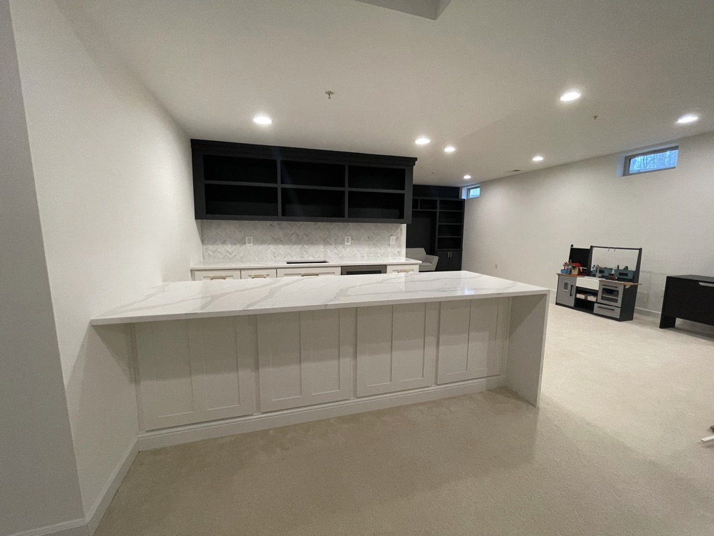 Completed wet bar with white quartz waterfall countertop and custom black upper cabinetry
