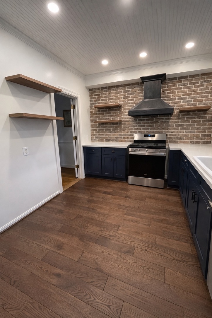 Completed kitchen with navy cabinets, brick veneer backsplash, custom hood, floating shelves, and hardwood flooring