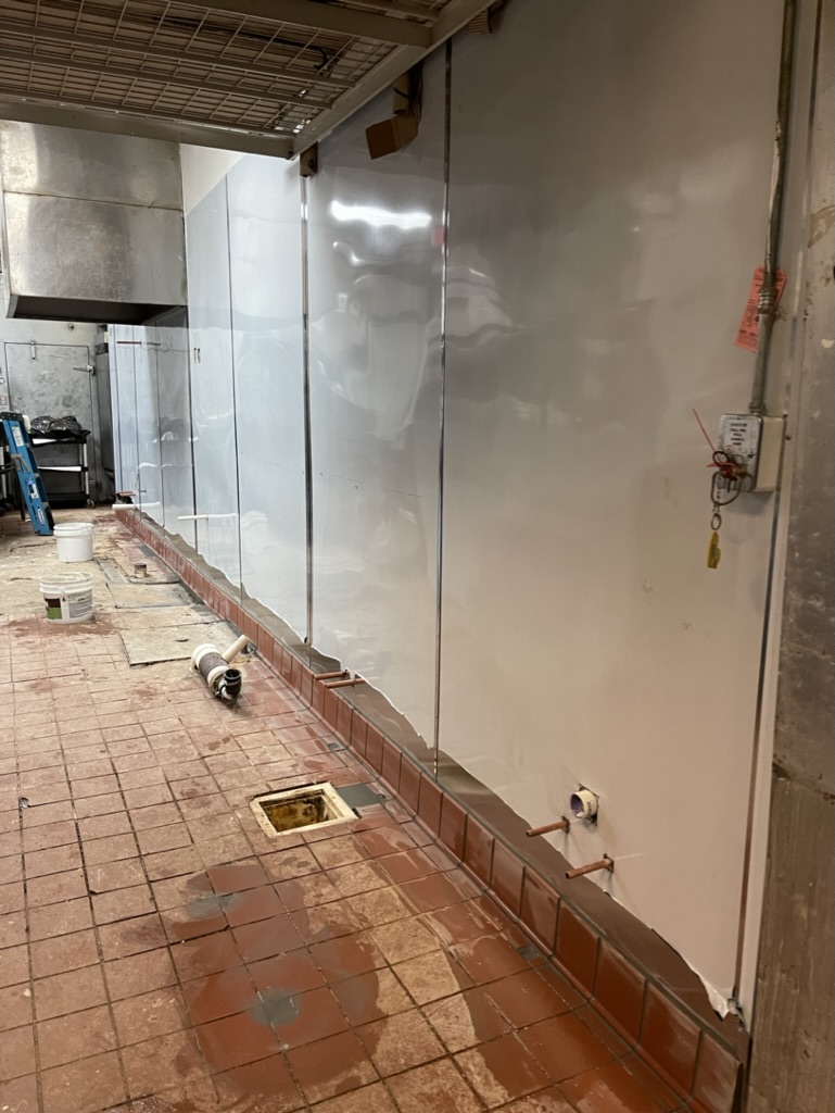 RESTORATION IN PROGRESS — Rebuilt wall with new stainless-steel panels and commercial base tile installed.