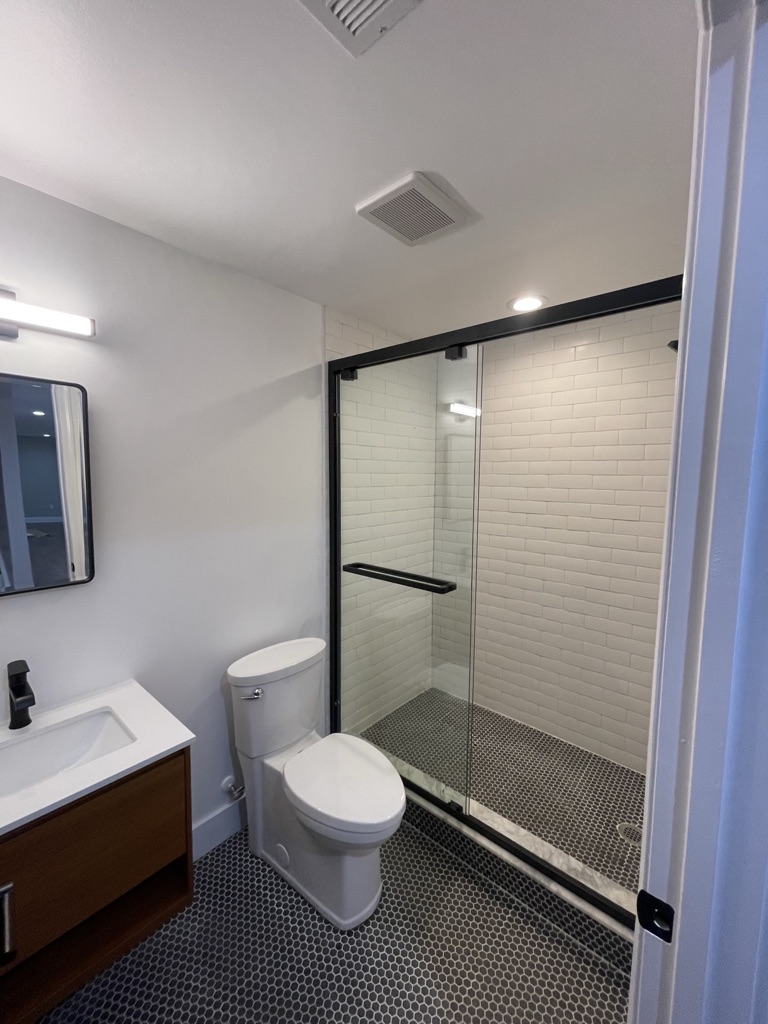 Modern basement bathroom with glass shower, white subway tile, and black fixtures