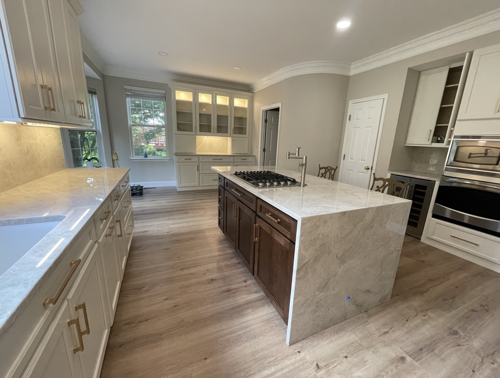 Completed waterfall quartz island with custom dark wood base, pot filler, glass display cabinetry, and seamless outlet-free backsplash