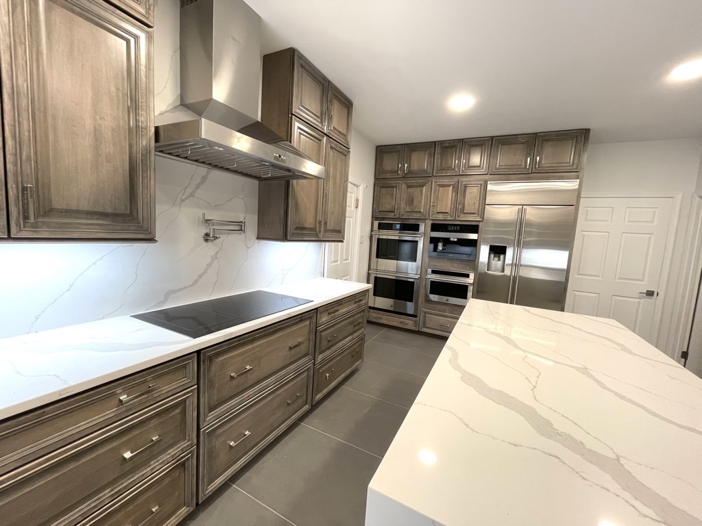 Finished range wall with custom hood, double ovens, pot filler, and quartz countertops
