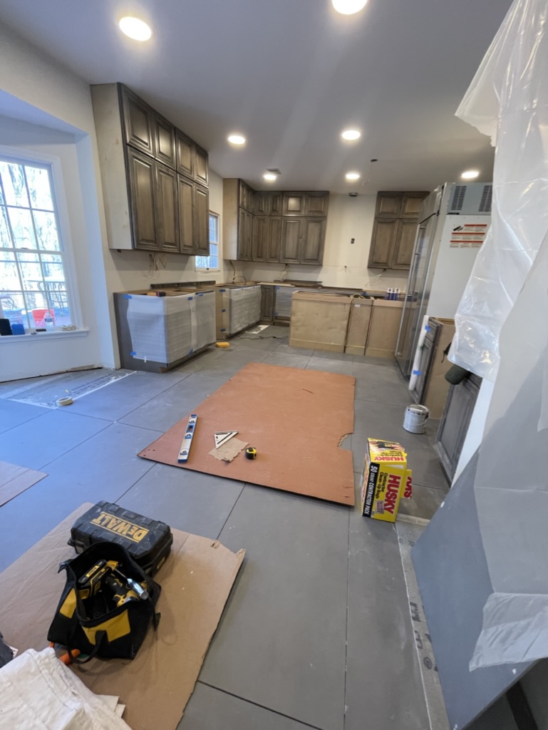 Construction in progress — custom cabinetry installed and large-format tile flooring being laid throughout the kitchen