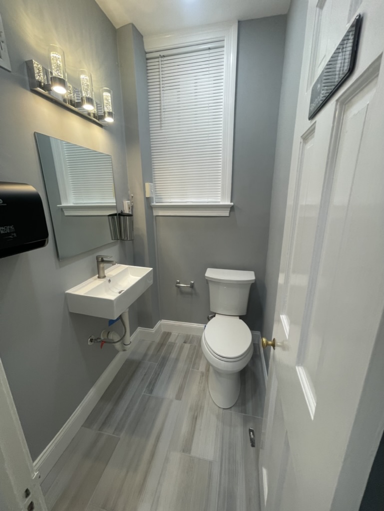 Renovated restroom with new tile flooring, fixtures, and vanity lighting